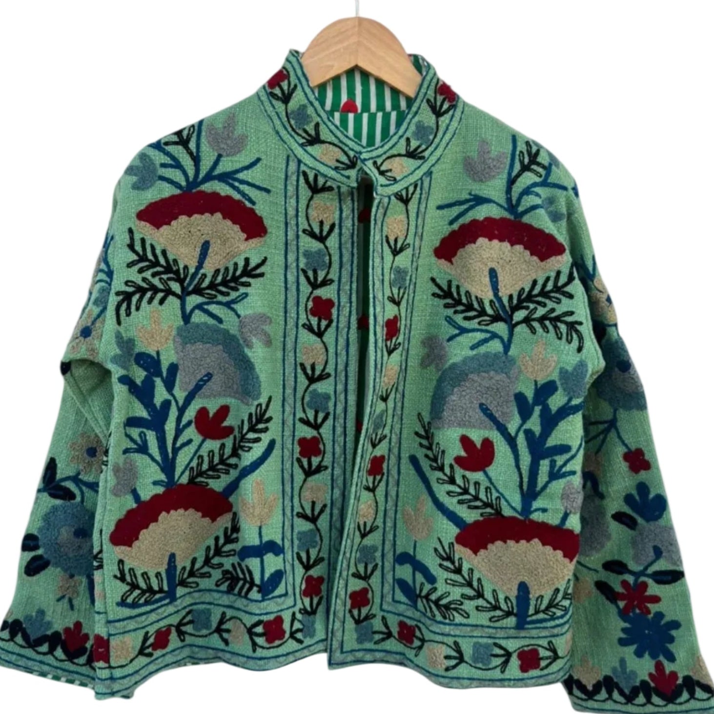Front view of an open-style handmade mint green textured cotton TNT jacket with colorful Suzani floral embroidery, showcasing a green-and-white striped interior lining dotted with small red hearts, isolated against a solid white background.