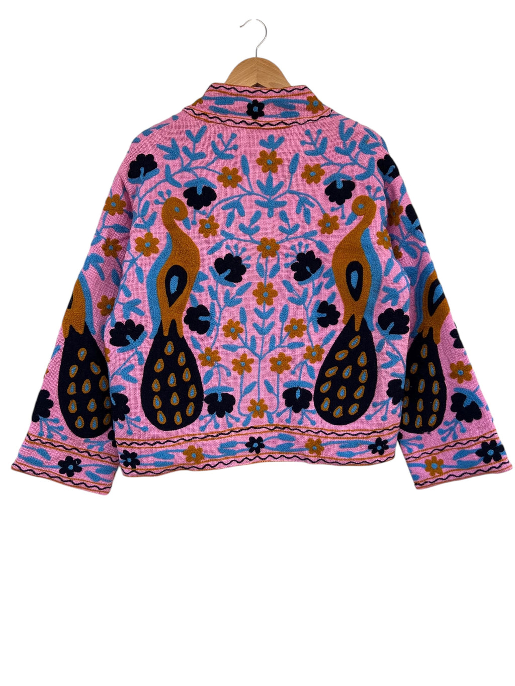 Front view of an open-style handmade bright pink textured cotton TNT jacket featuring Suzani embroidery of two majestic peacocks in gold and navy blue, showcasing a pink-and-white striped interior lining on the collar and folded cuffs, isolated on a solid white background.
