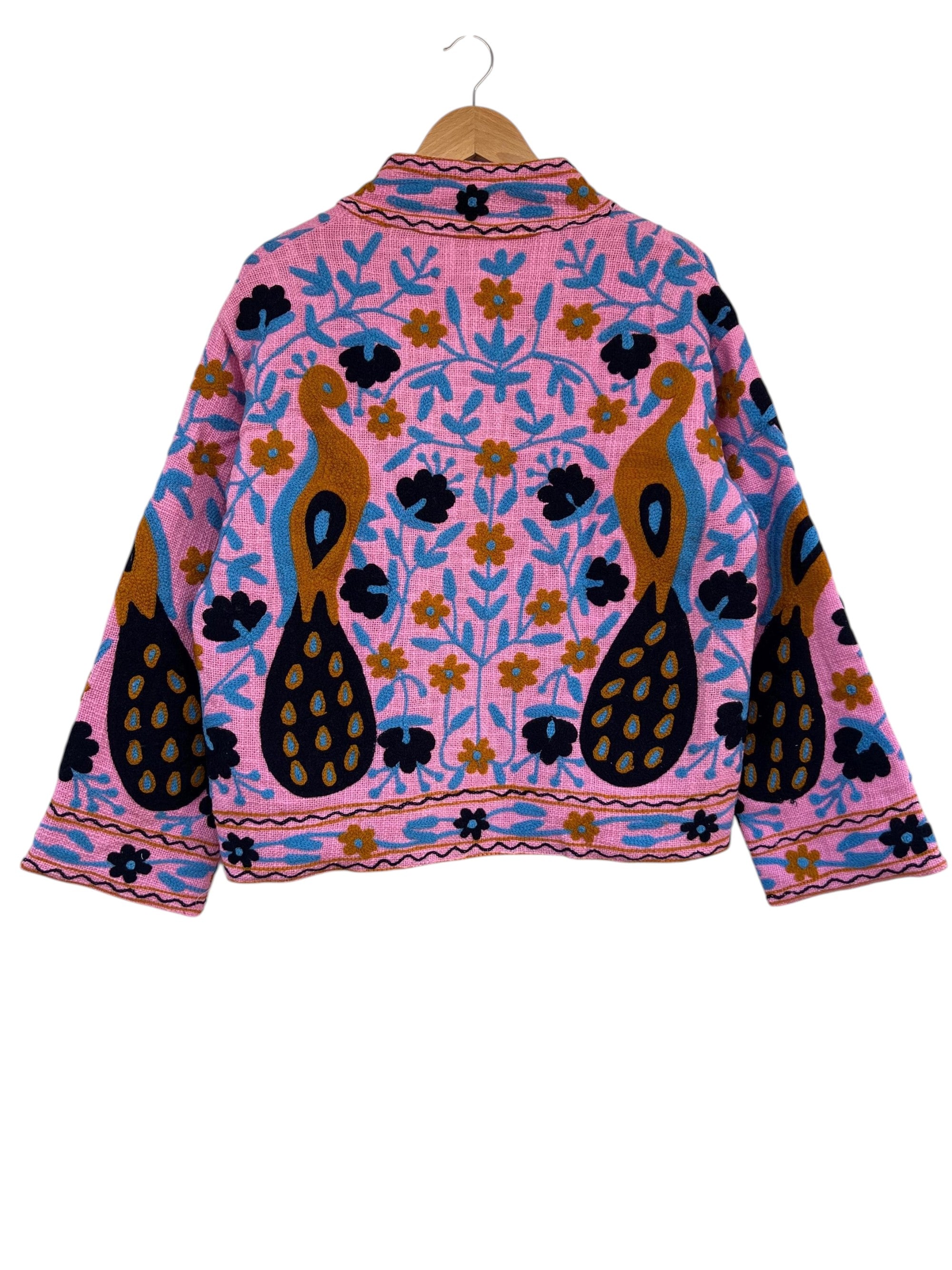 Front view of an open-style handmade bright pink textured cotton TNT jacket featuring Suzani embroidery of two majestic peacocks in gold and navy blue, showcasing a pink-and-white striped interior lining on the collar and folded cuffs, isolated on a solid white background.