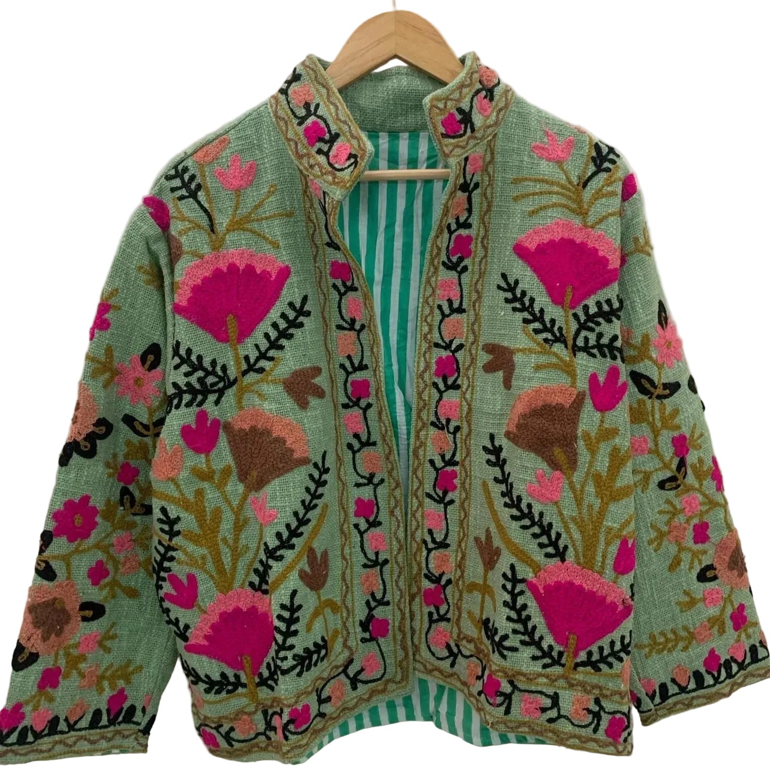 Front close-up of an open-style handmade mint green textured cotton TNT jacket featuring vibrant pinkish-red pomegranate and orange floral Suzani embroidery with thick dark green vines, hanging on a wooden hanger against a white wall.