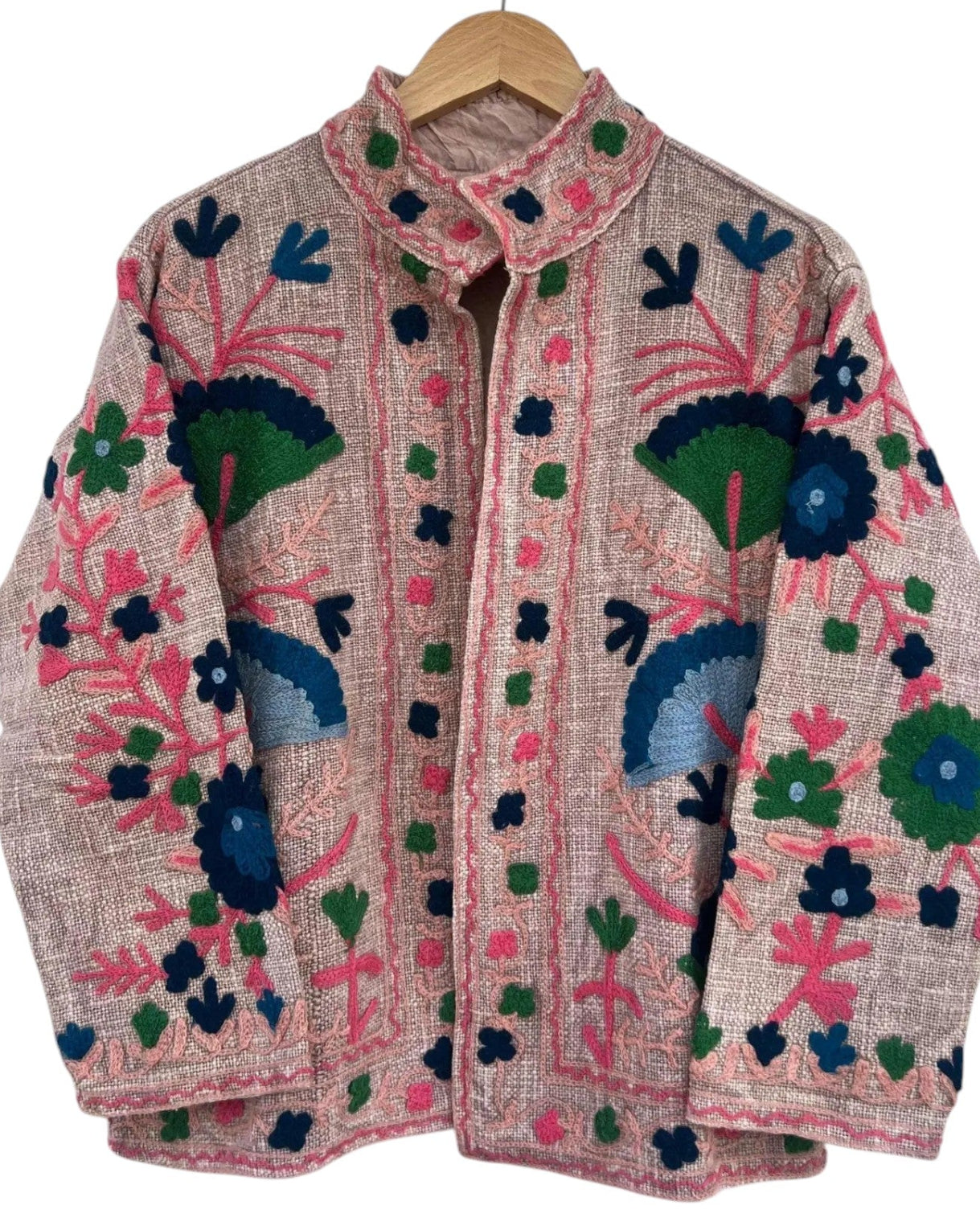 Light pink textured jacket featuring intricate, vibrant floral embroidery in hot pink, green, navy, and light blue, hanging on a wooden hanger.