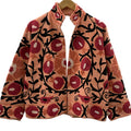 Front view of an open-style handmade peach textured cotton TNT short jacket featuring vibrant red pomegranate and orange floral Suzani embroidery with thick black vines, hanging on a wooden hanger against a white wall.