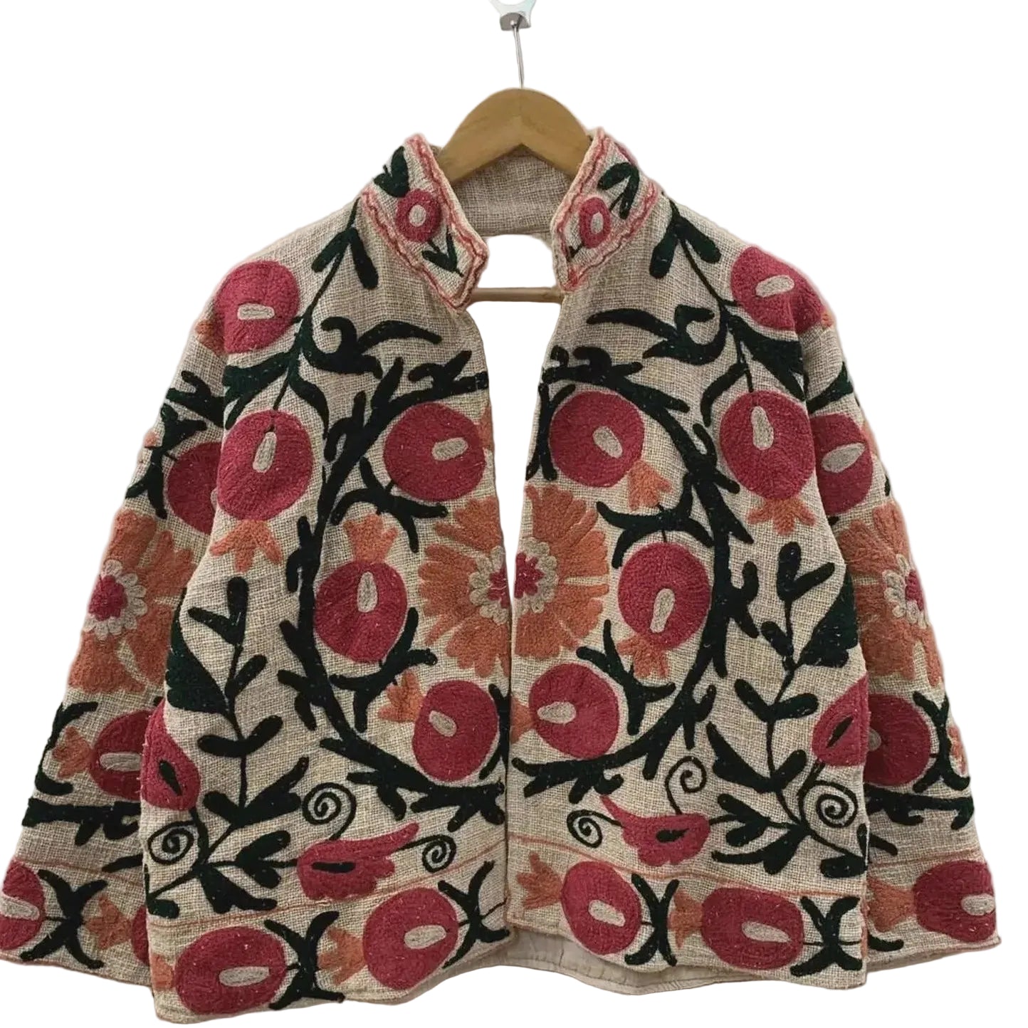 Front view of an open-style handmade beige textured cotton TNT short jacket featuring vibrant red pomegranate and orange floral Suzani embroidery with thick black vines, hanging on a wooden hanger against a white wall.