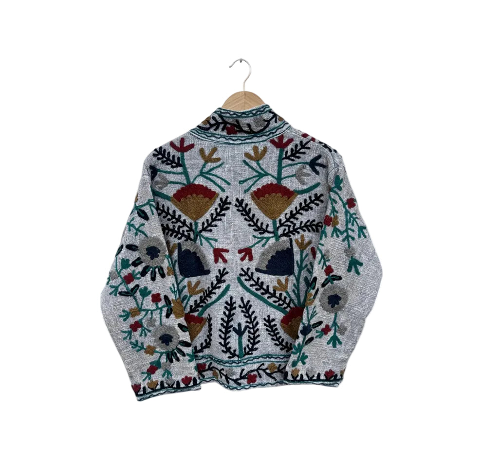 Back view of a light grey textured TNT jacket featuring symmetrical hand-embroidered geometric flowers in deep red, mustard gold, and dark green