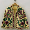 Front view of an open-style handmade pale yellow textured cotton TNT short jacket featuring large mauve paisley motifs, green leaves, and maroon Suzani floral embroidery, showcasing a matching solid yellow interior lining, hanging on a wooden hanger against a white wall.