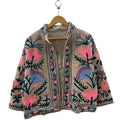 Front view of an open-style handmade beige textured cotton TNT short jacket featuring bright pink, periwinkle blue, and mauve Suzani floral embroidery with dark teal vines, showcasing a matching solid beige interior lining.