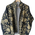Front view of an open-style handmade black textured cotton TNT short jacket featuring high-contrast metallic gold Suzani floral embroidery, showcasing a black-and-white striped interior lining, isolated on a light background.