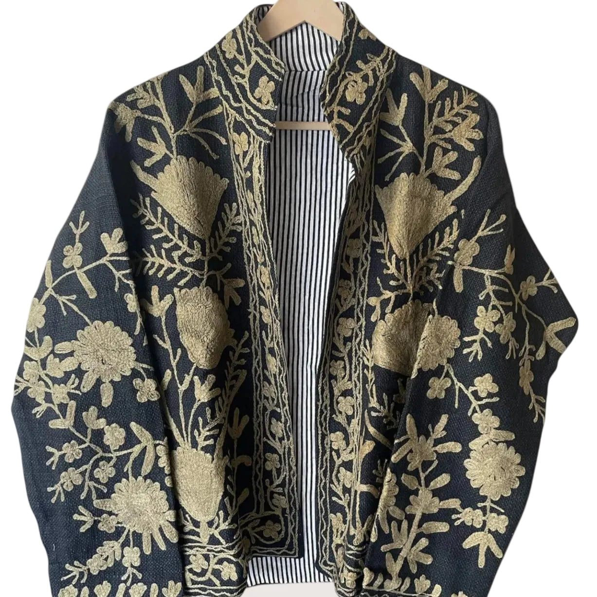 Front view of an open-style handmade black textured cotton TNT short jacket featuring high-contrast metallic gold Suzani floral embroidery, showcasing a black-and-white striped interior lining, isolated on a light background.