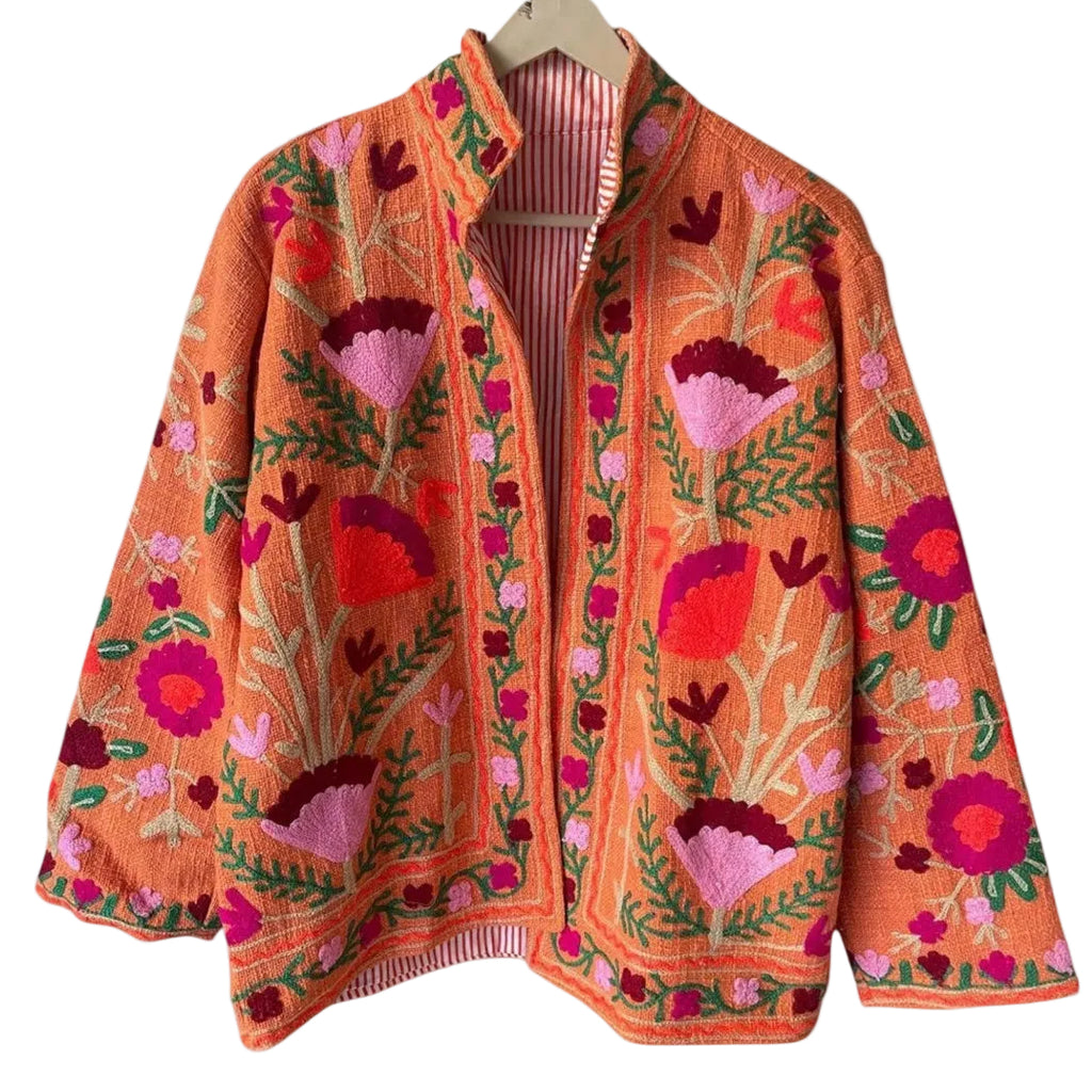 Front view of an open-style handmade orange textured cotton TNT jacket featuring vibrant pink and red Suzani floral embroidery with green vines, showcasing a red-and-white striped interior lining, isolated on a light background.