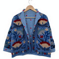 Front view of an open-style handmade denim-blue textured cotton TNT jacket with colorful Suzani floral embroidery, showcasing a blue-and-white striped interior lining dotted with small red hearts, isolated against a white background.