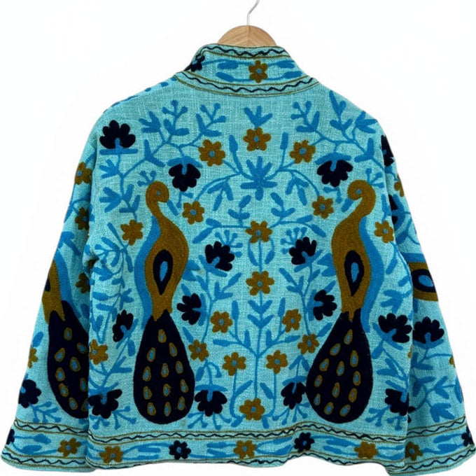 Back view of a handmade turquoise-blue textured cotton TNT short jacket featuring detailed mustard gold and navy blue Suzani embroidery of twin peacocks and floral vines, isolated on a solid white background.