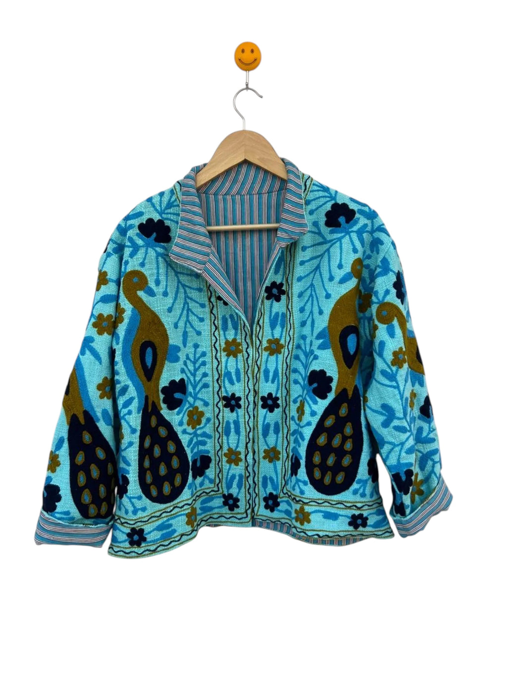 handmade turquoise-blue textured cotton TNT short jacket featuring detailed mustard gold and navy blue Suzani embroidery of twin peacocks and floral vines, isolated on a solid white background.