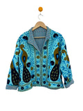 handmade turquoise-blue textured cotton TNT short jacket featuring detailed mustard gold and navy blue Suzani embroidery of twin peacocks and floral vines, isolated on a solid white background.