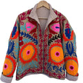 Front view of a handmade beige textured cotton TNT short jacket featuring ultra-bright multi-colored Suzani embroidery with large orange and pink floral medallions, showcasing a brown-and-white striped interior lining on the collar and folded cuffs, isolated against a solid white background.