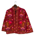 Deep red open-front TNT jacket featuring symmetrical pink, purple, and yellow floral embroidery with a detailed stitched border, hanging on a wooden hanger.