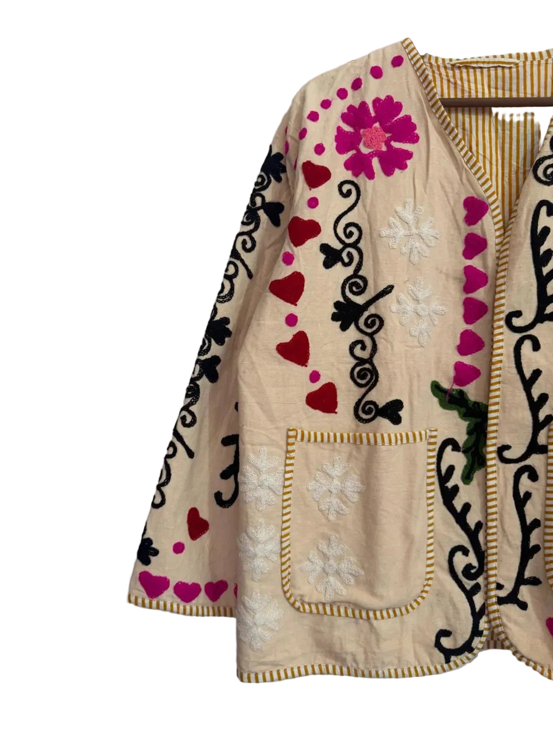 Front view of a cream-colored open-front TNT jacket featuring colorful embroidery including bright pink hearts, black vines, pink flowers, and white starbursts, finished with yellow and white striped piping and two front patch pockets.