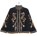 Close up of a black open-front TNT jacket featuring symmetrical peach, blush pink, and olive green swirling embroidery, highlighted by a bold black-and-white striped lapel and inner lining.