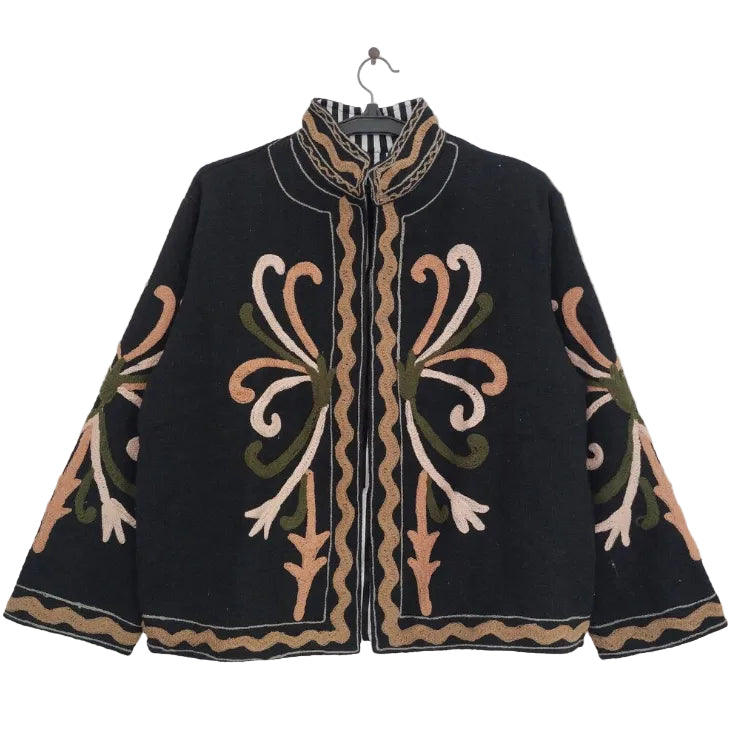 Close up of a black open-front TNT jacket featuring symmetrical peach, blush pink, and olive green swirling embroidery, highlighted by a bold black-and-white striped lapel and inner lining.