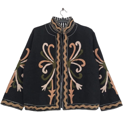 Close up of a black open-front TNT jacket featuring symmetrical peach, blush pink, and olive green swirling embroidery, highlighted by a bold black-and-white striped lapel and inner lining.