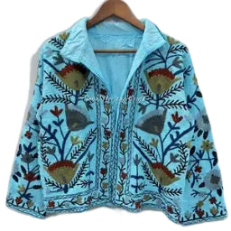 A vibrant sky blue hand-embroidered Suzani jacket with olive green, navy blue, and rust red floral botanical patterns hanging on a wooden hanger .