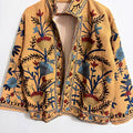 Back view of a mustard yellow TNT jacket featuring intricate symmetrical navy blue, light blue, and deep red floral and vine embroidery.