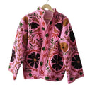 Light pink bohemian TNT jacket featuring oversized dark brown floral embroidery, green vine details, and an open front, hanging against a textured white wall.