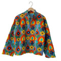 Front view of an open-style handmade periwinkle blue textured cotton TNT short jacket featuring a dense, all-over pattern of bright orange, yellow, and green Suzani floral embroidery.